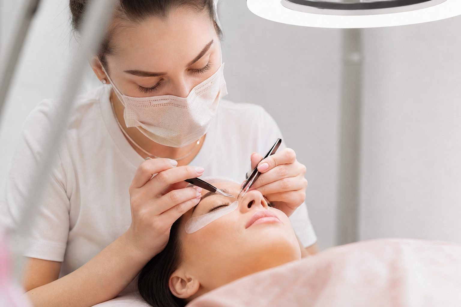 Close view of a lash artist isolating a natural lash with fine tweezers under a bright ring light